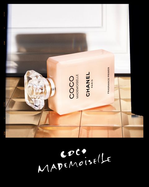 Ein rechteckiger Flakon des Parfums Coco Mademoiselle Chanel Paris mit einem facettierten Verschluss liegt auf goldenen Fliesen und lehnt an einer weißen Wand. Der Markenname und die Produktangaben sind in schwarzer Farbe auf den Flakon gedruckt.