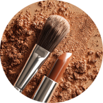 Ein Schminkpinsel und ein brauner Lippenstift auf einer strukturierten Oberfläche aus losem braunem Puder, von oben gesehen.