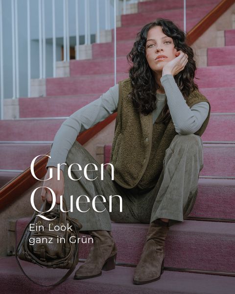 Eine Frau mit gewelltem dunklem Haar sitzt auf einer Treppe mit rosa Teppichboden und trägt eine grüne Cordhose, ein grünes langärmeliges Oberteil, eine grüne Weste und braune Stiefel. Der Text lautet: "Grüne Königin. Ein Look ganz in Grün.