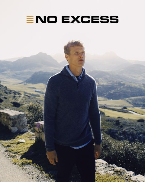 Ein Mann in einem blauen Pullover steht an einem sonnigen Tag im Freien, mit Bergen und Tälern im Hintergrund. Die Worte "NO EXCESS" erscheinen in fetten Buchstaben am oberen Rand des Bildes.