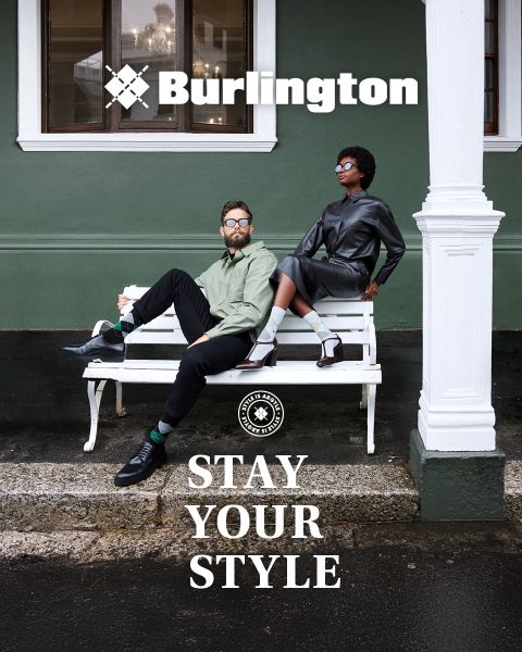 Ein Mann und eine Frau in stilvollen Outfits posieren selbstbewusst auf einer weißen Bank vor einer grünen Wand mit den Texten "Burlington" und "Stay Your Style" über und unter ihnen.