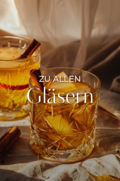 Zwei Kristallgläser, gefüllt mit einem goldenen Getränk und garniert mit Zimtstangen, stehen auf einer leichten Stoffoberfläche. Der Text "ZU ALLEN Gläsern" überlagert das Bild. Die warme Beleuchtung unterstreicht die gemütliche Atmosphäre.