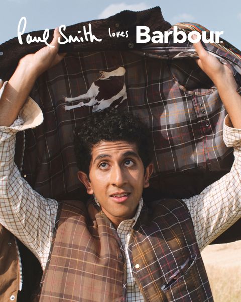 Ein Mann hält eine karierte Jacke über seinem Kopf offen und schaut mit einem leichten Lächeln nach oben. Der Text "Paul Smith loves Barbour" steht am oberen Rand des Bildes.