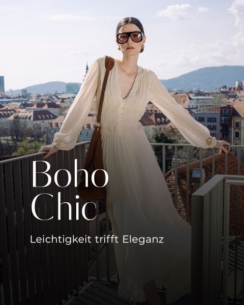 Eine Frau in einem fließenden cremefarbenen Kleid und einer Sonnenbrille steht auf einem Balkon mit Blick auf eine Stadt, mit Text: "Boho Chic. Leichtigkeit trifft Eleganz.