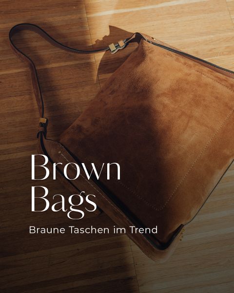 Eine große braune Wildleder-Umhängetasche mit goldenen Beschlägen liegt auf einem Holzboden. Der Text lautet "Brown Bags" und "Braune Taschen im Trend".
