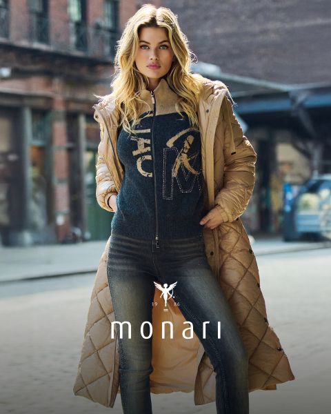 Eine Frau mit langen blonden Haaren trägt einen hellbraunen Steppmantel über einem dunklen Pullover und Jeans und steht selbstbewusst auf einer Stadtstraße. Das Wort "monari" ist am unteren Rand des Bildes eingeblendet.