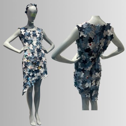 Zwei Schaufensterpuppen zeigen ein ärmelloses Kleid aus sich überlappenden Stoffpuzzleteilen in verschiedenen Blau- und Grautönen mit einem asymmetrischen Saum.