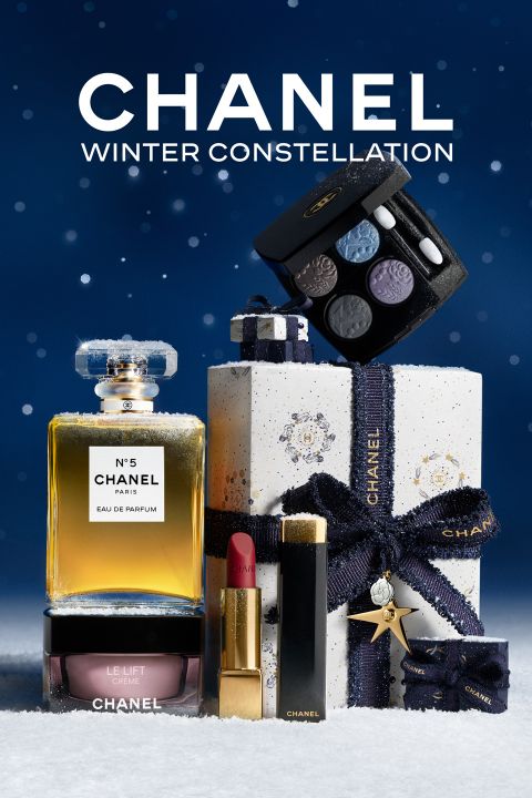 Chanel-Parfüm, Lippenstift, Creme, Lidschatten und eine Geschenkschachtel mit einem Sternenband vor einem verschneiten Sternenhintergrund mit dem Text "CHANEL".