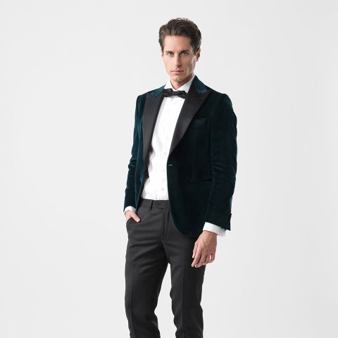 Mann mit dunkelgrüner Samtjacke, weißem Hemd, schwarzer Fliege und schwarzer Hose vor einem schlichten weißen Hintergrund.