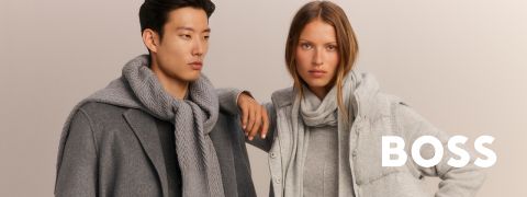 Ein Mann und eine Frau in stilvoller grauer Winterkleidung mit Schals stehen nebeneinander; in weißer Schrift steht "BOSS".