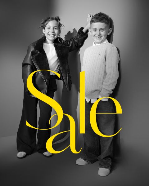 Zwei lächelnde Kinder posieren in schicken Outfits mit dem Wort "Sale" in großen gelben Buchstaben über dem Bild.