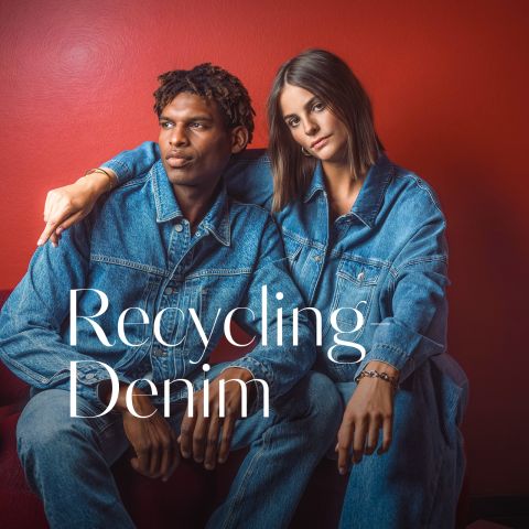 Zwei Personen in Jeansjacken und Jeans sitzen vor einer roten Wand. Auf dem Bild steht: „Recycling Denim.“.