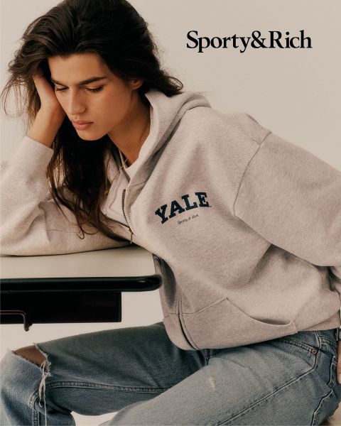 Eine Person in einem grauen YALE-Kapuzenpullover und zerrissenen Jeans sitzt an einem Tisch und schaut nachdenklich nach unten. In der oberen rechten Ecke steht "Sporty & Rich".
