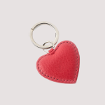 Ein roter herzförmiger Schlüsselanhänger aus Leder mit sichtbaren Nähten und einem silbernen Schlüsselring vor einem hellen Hintergrund.