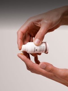 Eine Person gibt eine kleine Menge Creme oder Lotion aus einer weißen Flasche auf ihre Fingerspitze.