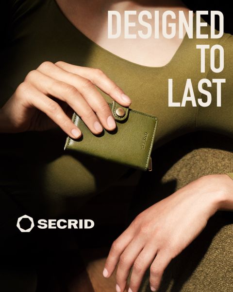 Eine Frau in einem olivgrünen Kleid hält eine passende Secrid-Brieftasche. Der Text lautet: "DESIGNED TO LAST" und das Secrid-Logo ist zu sehen.