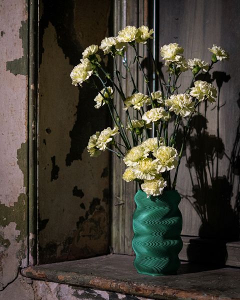 Gelbe Nelken in einer strukturierten grünen Vase stehen auf einer verwitterten Fensterbank mit abblätternder Farbe und gealterten Holzplatten im Hintergrund.