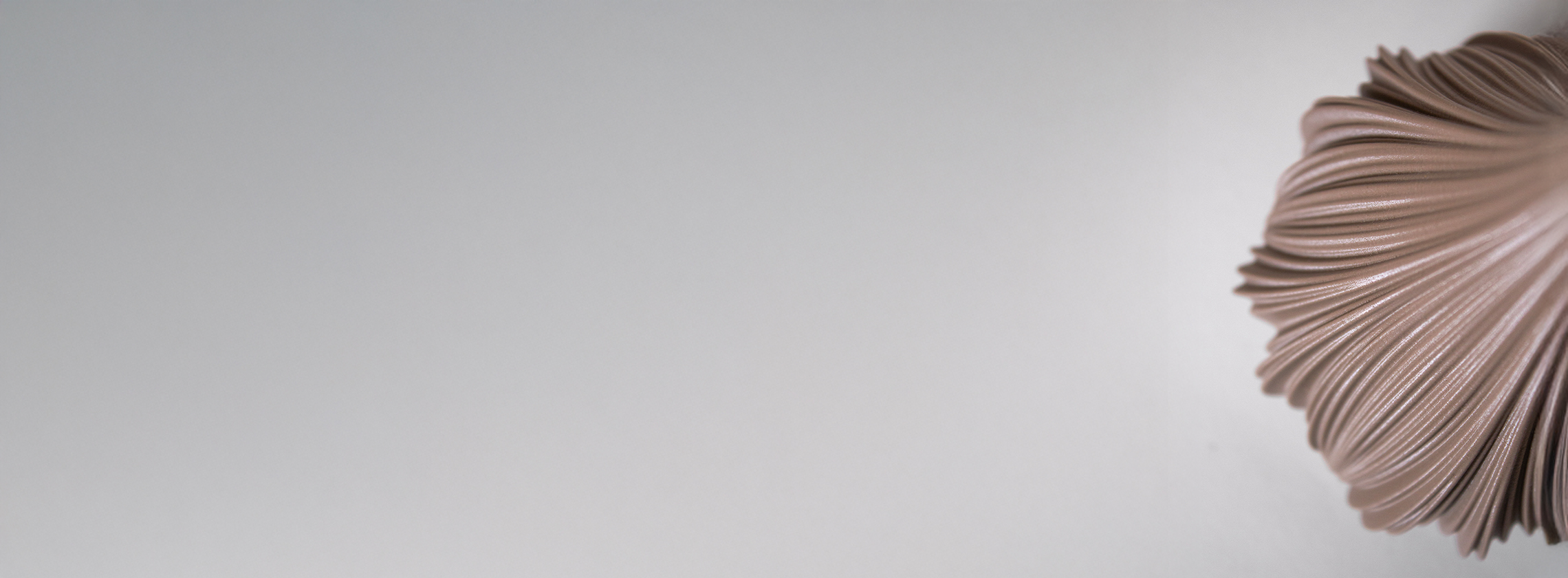 Texturierte, rosafarbene Keramikvase, die teilweise auf der rechten Seite eines hellgrauen Hintergrunds zu sehen ist, mit viel freiem Raum auf der linken Seite.