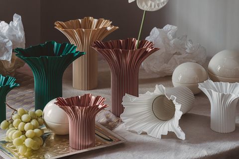 Auf einem Tisch stehen mehrere skulpturale Vasen in verschiedenen Farben und Größen, daneben Weintrauben, weiße Keramikkugeln und zerknülltes Papier.