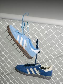 Zwei blaue Adidas-Turnschuhe mit weißen Streifen hängen an ihren Schnürsenkeln an einem weißen Metallzaun, einer hellblau und einer dunkelblau.