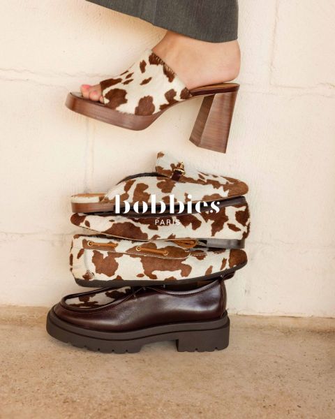 Vier modische Schuhe, darunter Absätze mit Kuhdruck, Slipper und ein dunkelbrauner, klobiger Schuh, gestapelt vor einer hellen Wand mit Textüberlagerung "Bobbies Paris".