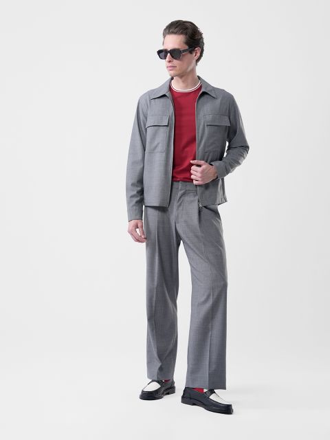 Mann mit Sonnenbrille, grauem Anzug, rotem Hemd, schwarz-weißen Schuhen und einer Halskette, vor weißem Hintergrund.