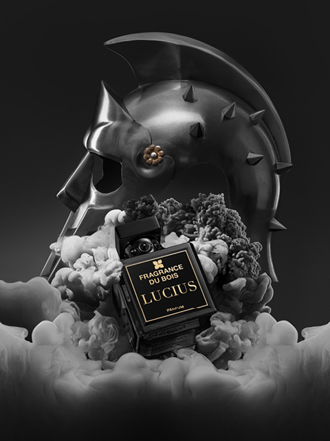 Inmitten von Rauch steht ein schwarzer Parfümflakon mit der Aufschrift „Fragrance Du Bois Lucius“, im Hintergrund ist ein metallener Gladiatorenhelm zu sehen.