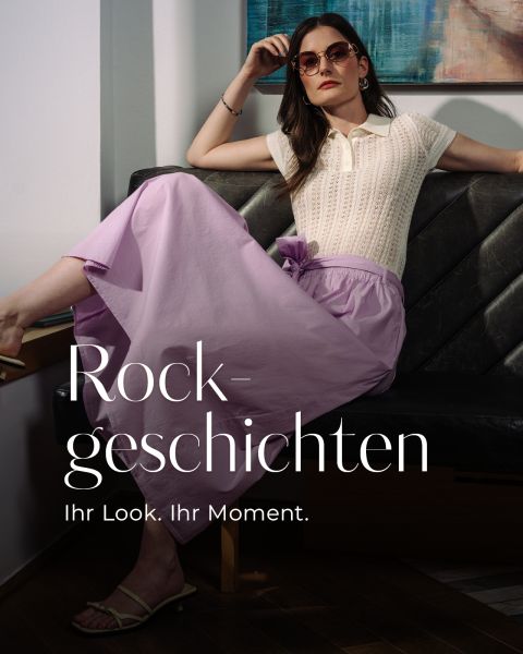 Eine Frau in einem weißen Strickoberteil und einem fließenden lilafarbenen Rock, die eine Sonnenbrille trägt und auf einer dunklen Couch sitzt, mit überlagertem Text.