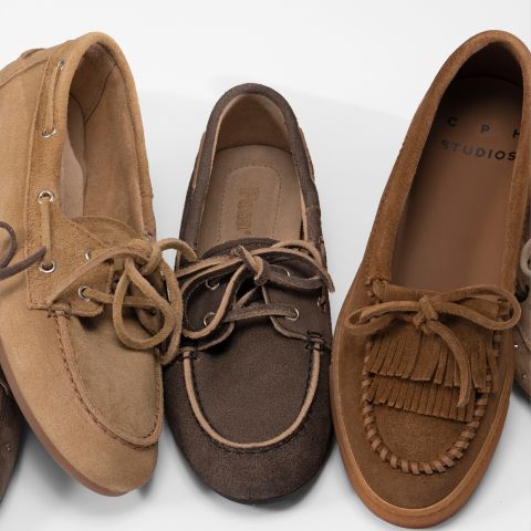 Drei braune Veloursleder-Slipper mit Schnürsenkeln sind nebeneinander angeordnet und weisen jeweils unterschiedliche Nähte und Details auf weißem Grund auf.