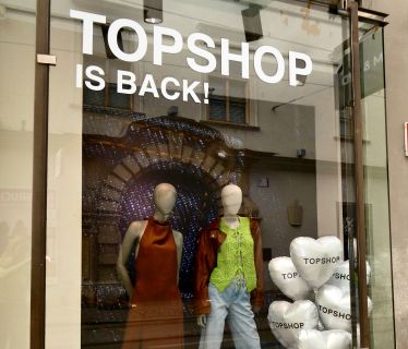 Schaufenster mit "TOPSHOP IS BACK!"-Schild, zwei Schaufensterpuppen in trendigen Outfits und weißen herzförmigen Luftballons mit dem Aufdruck "TOPSHOP".