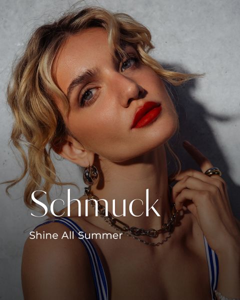 Eine Frau mit gewelltem blondem Haar, kräftigem roten Lippenstift und Goldschmuck posiert im Sonnenlicht. Der Text lautet: "Schmuck. Shine All Summer.