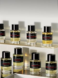 Auf gestuften Regalen sind neun Flakons mit Parfüm von Frederic Malle ausgestellt, die jeweils einen schwarzen Verschluss und ein Etikett mit dem Namen des Duftes tragen.