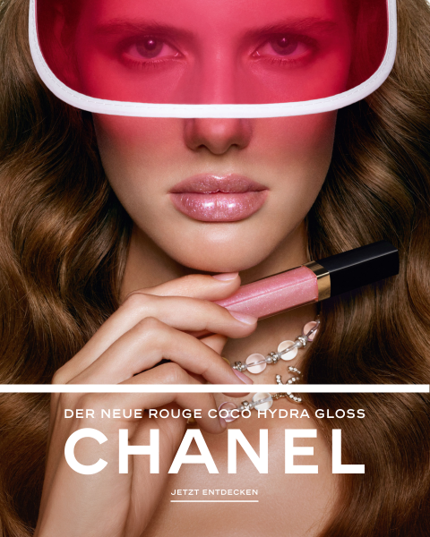 Eine Frau mit welligem braunem Haar trägt ein rosa Visier und eine Perlenkette und hält einen rosa Chanel-Lipgloss in der Hand. Text: „CHANEL, der neue Rouge Coco Hydra Gloss.“.