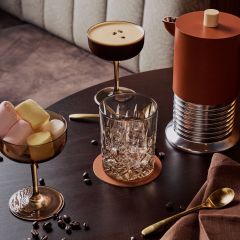 Ein Tisch mit einem Cocktail, einem Glas, einer Schale mit Marshmallows, einer Kaffeekanne, einem goldenen Löffel, einer Serviette und verstreuten Kaffeebohnen.