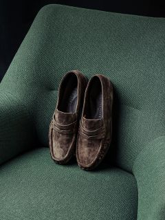 Ein Paar braune Wildleder-Loafer liegt ordentlich auf einem grün gepolsterten Sessel.