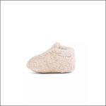Ein einzelner beiger, flauschiger Babyschuh ist vor einem schlichten weißen Hintergrund abgebildet.