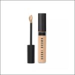 Eine Tube Bobbi Brown Concealer mit schwarzer Kappe, abgebildet mit herausgezogenem Applikator, der den beigen Concealer zeigt.