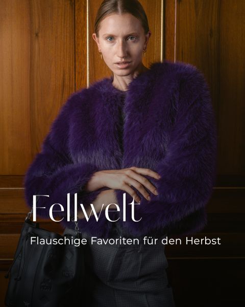 Eine Frau in einem violetten Kunstpelzmantel steht in einem Raum und hält eine schwarze Tasche in der Hand. Der Text lautet: „Fellwelt. Flauschige Favoriten für den Herbst.“.