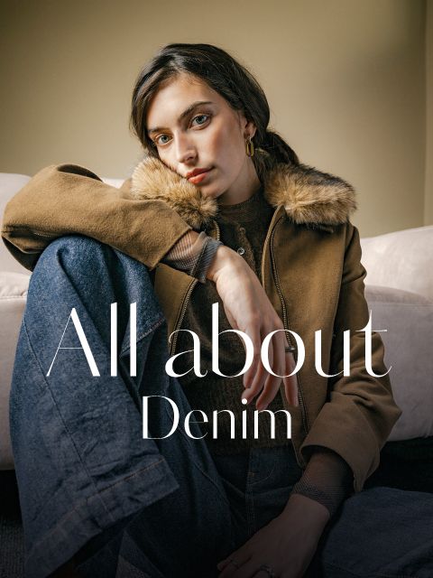 Eine Frau, die eine braune Jacke mit pelzbesetztem Kragen und Jeans trägt, über der der Schriftzug „All about Denim“ zu sehen ist.
