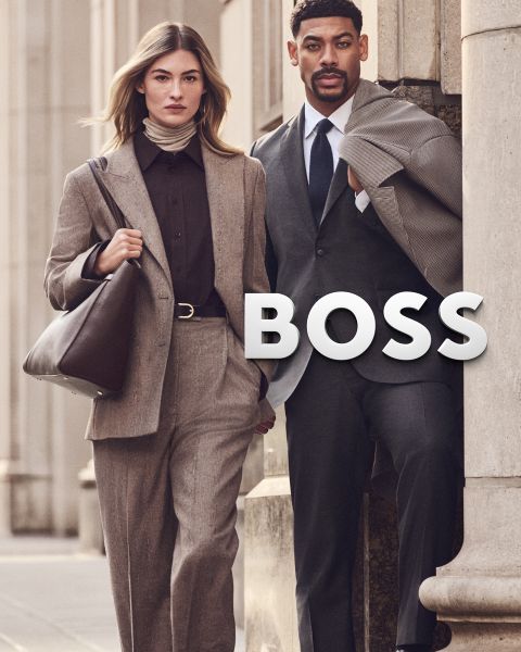 Eine Frau und ein Mann in professioneller Geschäftskleidung stehen im Freien neben dem Wort „BOSS“.