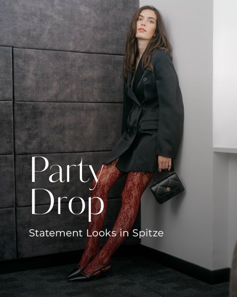 Eine Frau in einem schwarzen Blazer und roten Spitzenstrumpfhosen trägt eine kleine schwarze Handtasche. Textüberlagerung: „Party Drop. Statement-Looks aus Spitze.“